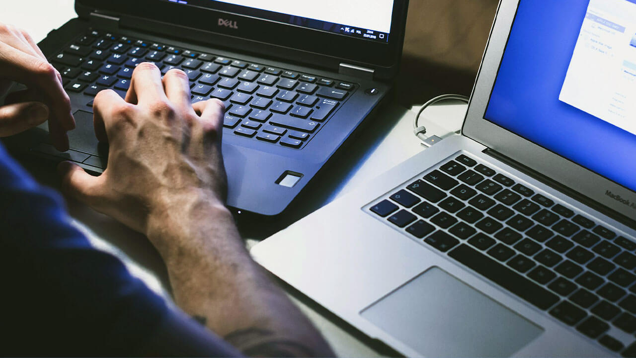 DELLのノートパソコンとMacBookを並べて操作する男性